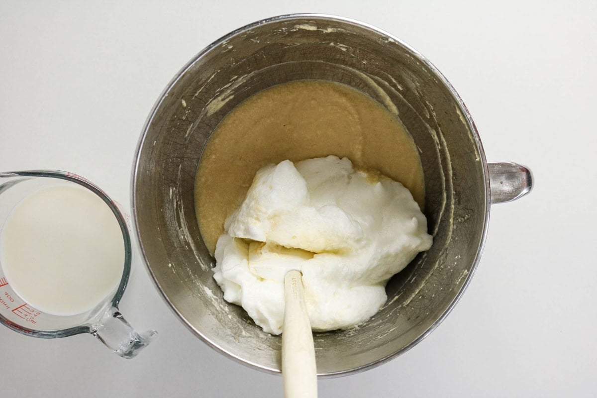 Metal bowl with batter, whipped egg whites, and a measuring cup of milk nearby.