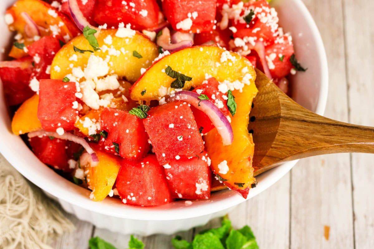 Watermelon and peach salad with feta, red onion, and mint in a white bowl.