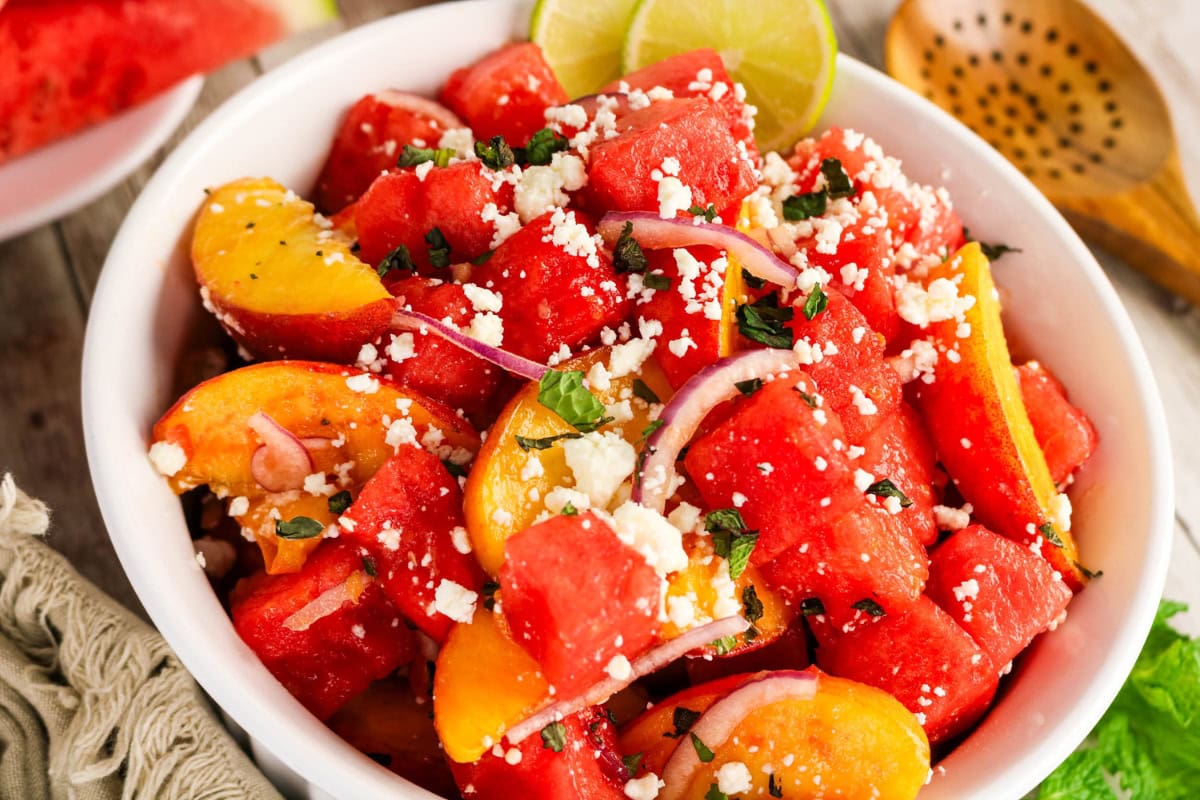 Bowl of watermelon, peaches, red onion, feta, herbs, and lime slices.