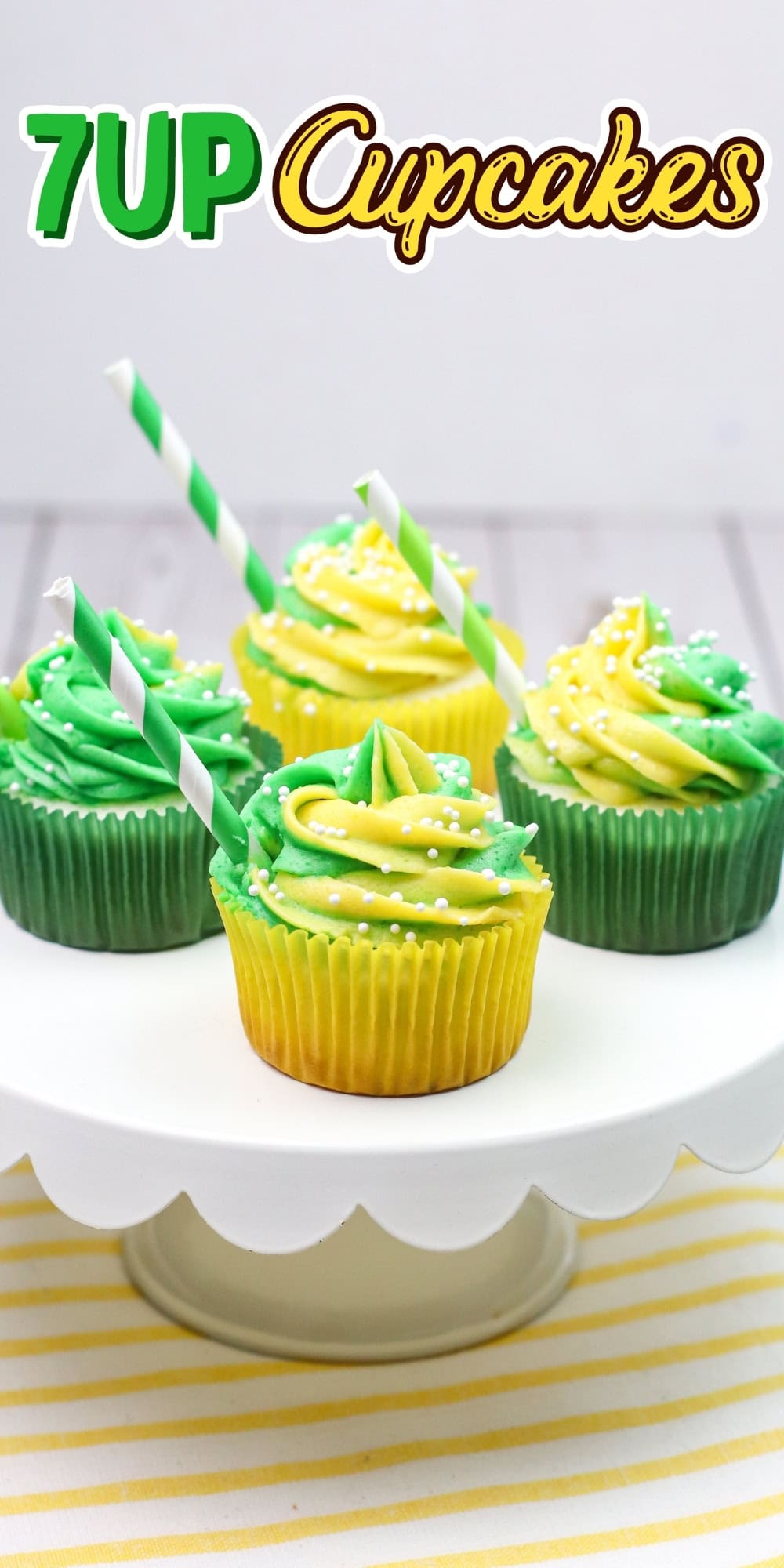 Green and yellow frosted cupcakes with straws on a white cake stand.
