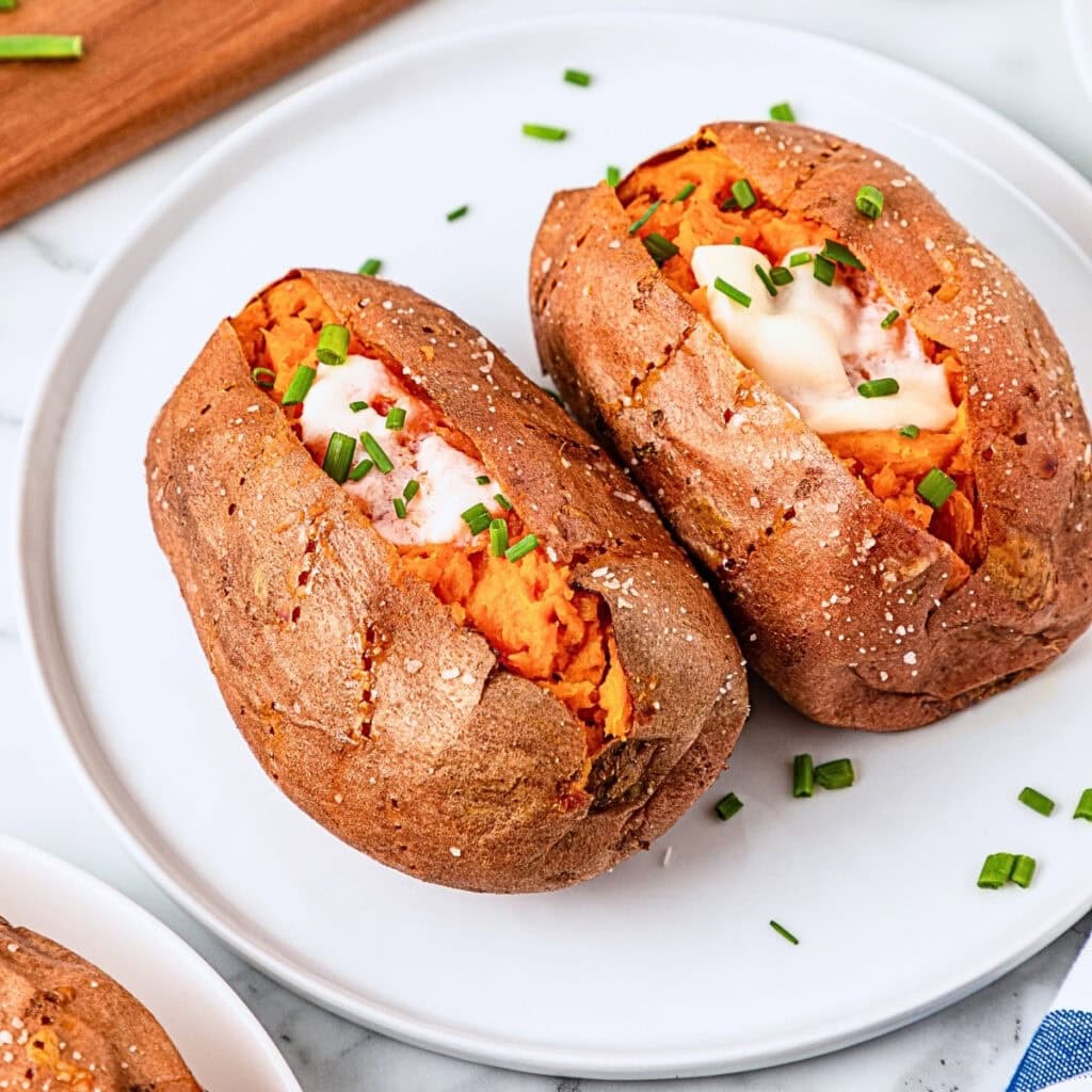 Two baked sweet potatoes with sour cream and chives on a white plate.