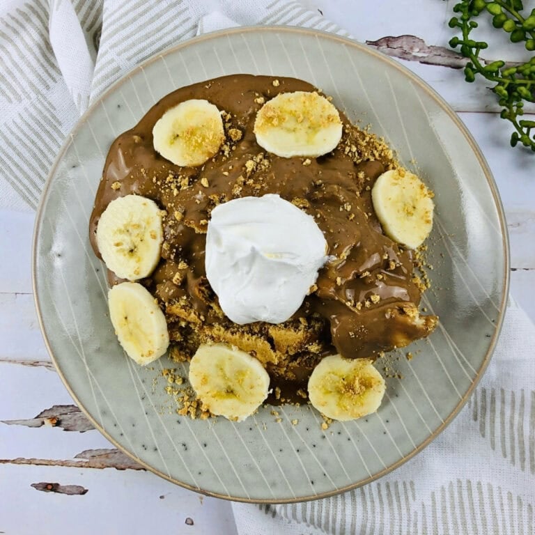 Pancake topped with chocolate, banana slices, crumbs, and whipped cream.