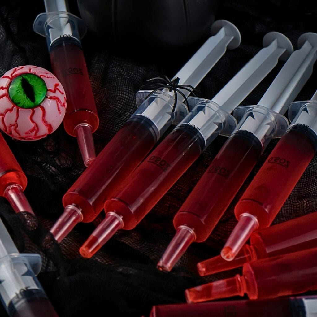 Red liquid-filled syringes and a fake eyeball on black fabric background.