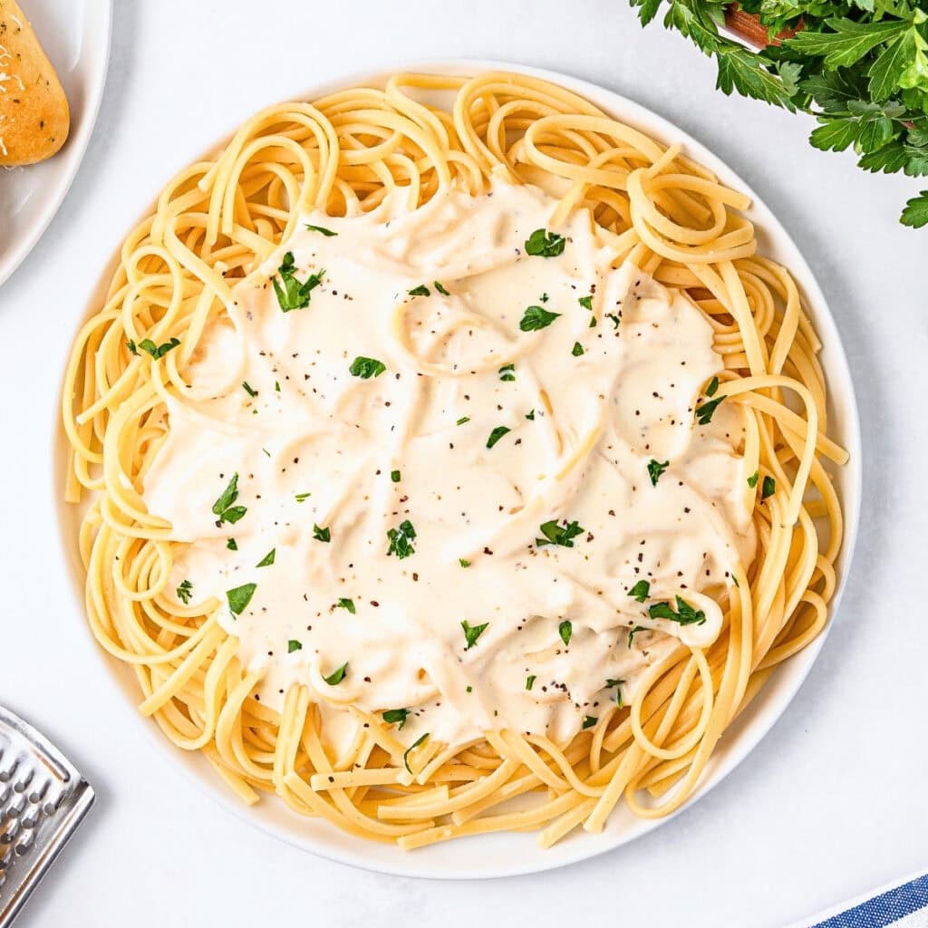Spaghetti with creamy white sauce, garnished with parsley and black pepper.