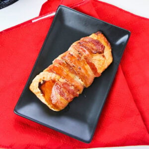 Bacon-wrapped pastry on a black plate, set on a red napkin.
