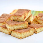 Cinnamon sugar bars stacked on a white plate with a colorful napkin behind.