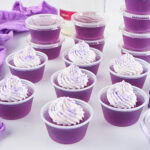 Purple gelatin cups with whipped cream and sprinkles on top, neatly arranged.