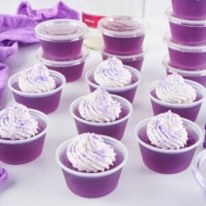 Purple gelatin cups with whipped cream and sprinkles on top, neatly arranged.