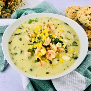 Creamy soup with shrimp, corn, and herbs in a white bowl on a towel.