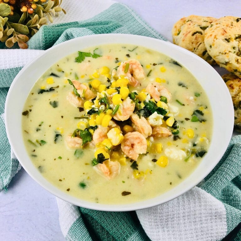 Creamy soup with shrimp, corn, and herbs in a white bowl on a towel.