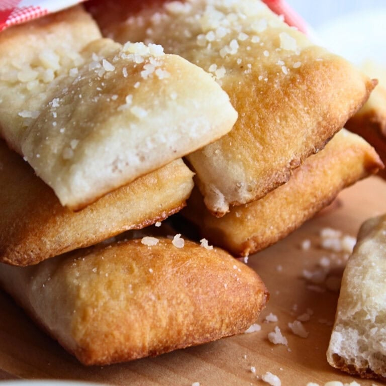 Golden brown breadsticks topped with coarse salt on a wooden surface.