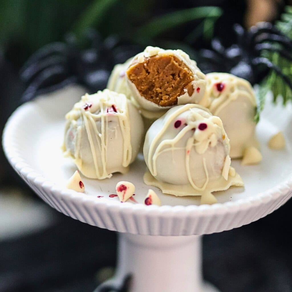 White chocolate truffles with a bite taken, on a white cake stand.