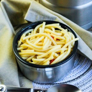 Cooked spaghetti in a metal bowl on a beige napkin with a silver spoon nearby.