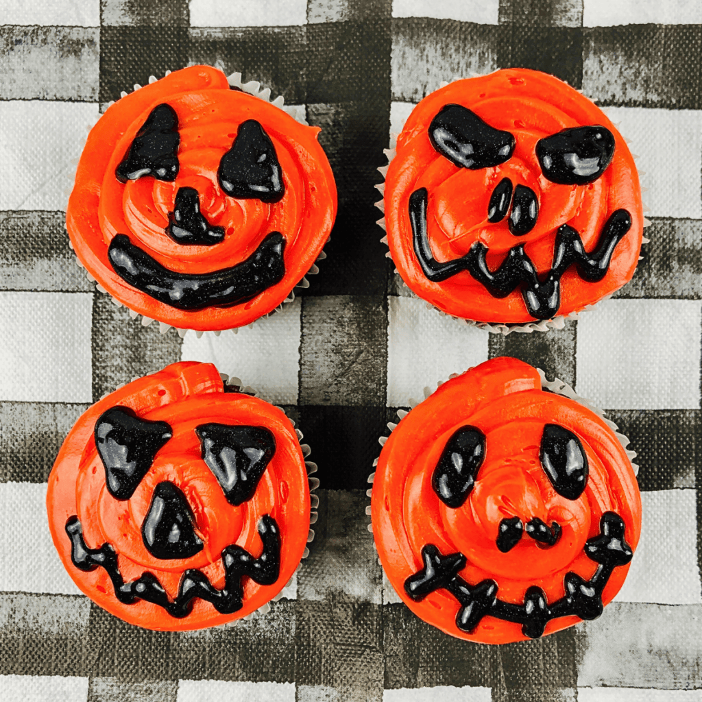 Four cupcakes decorated as orange jack-o-lanterns with black frosting faces.