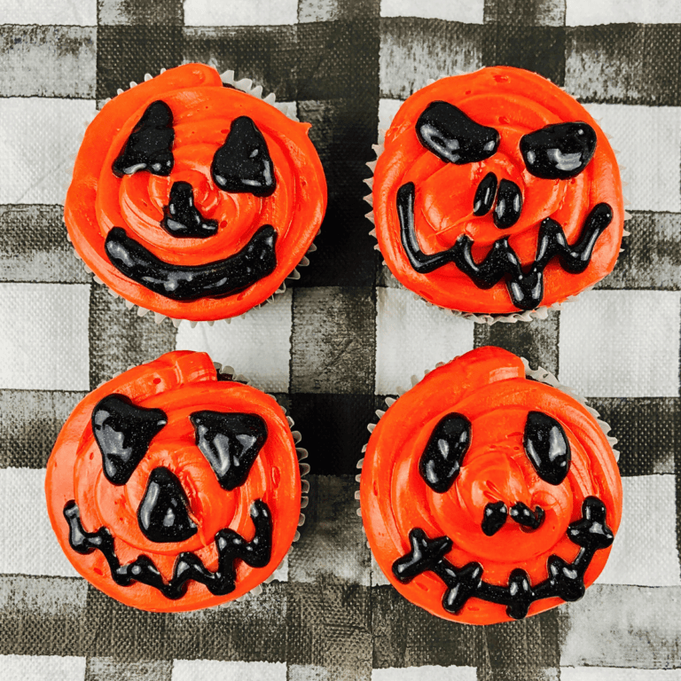 Four cupcakes decorated as orange jack-o-lanterns with black frosting faces.
