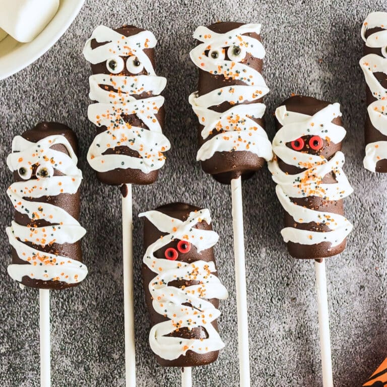 Five chocolate mummy pops with candy eyes and white drizzle on sticks.
