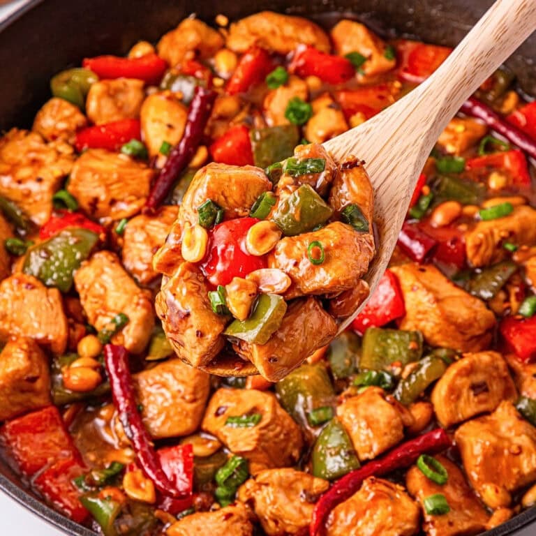 Wooden spoon scooping spicy stir-fried chicken with peppers and peanuts.