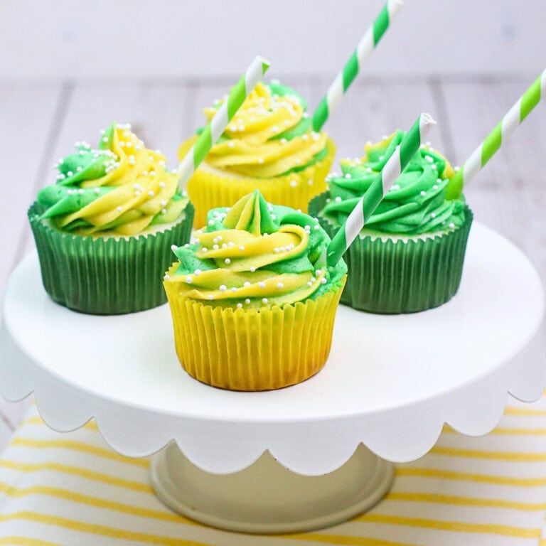 Four green and yellow cupcakes with striped straws on a white cake stand.