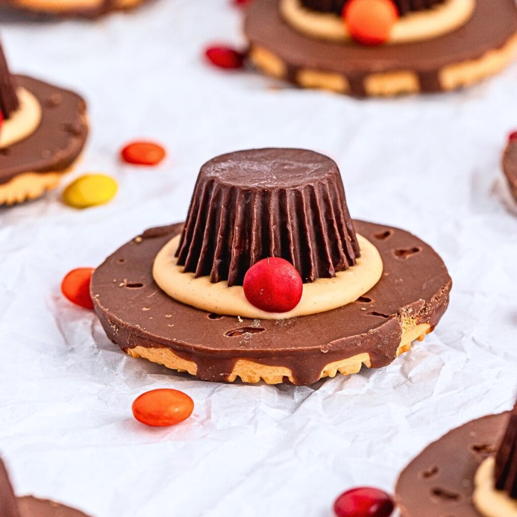 Chocolate peanut butter pilgrim hat cookie with candy decoration on parchment.
