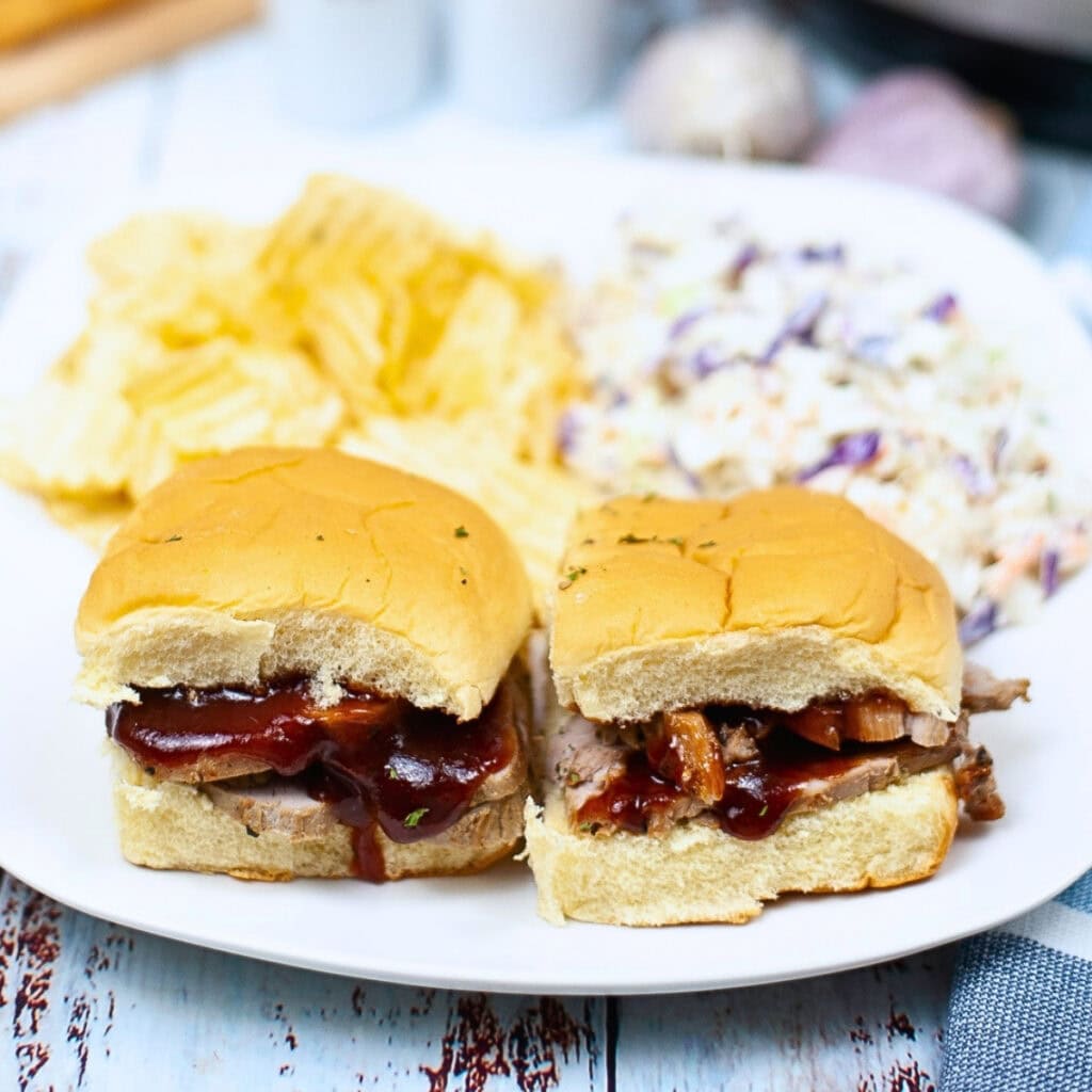 Two BBQ pork sliders with chips and coleslaw on a white plate.