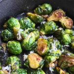 Brussels sprouts sautéed in a pan with grated cheese on top.