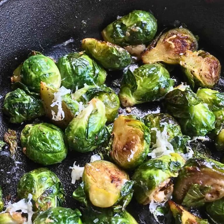 Brussels sprouts sautéed in a pan with grated cheese on top.