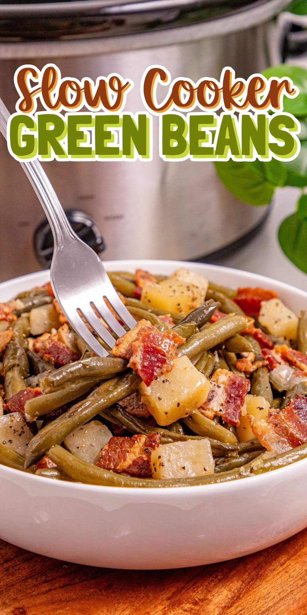 Bowl of green beans, potatoes, and bacon with a fork, slow cooker in background.