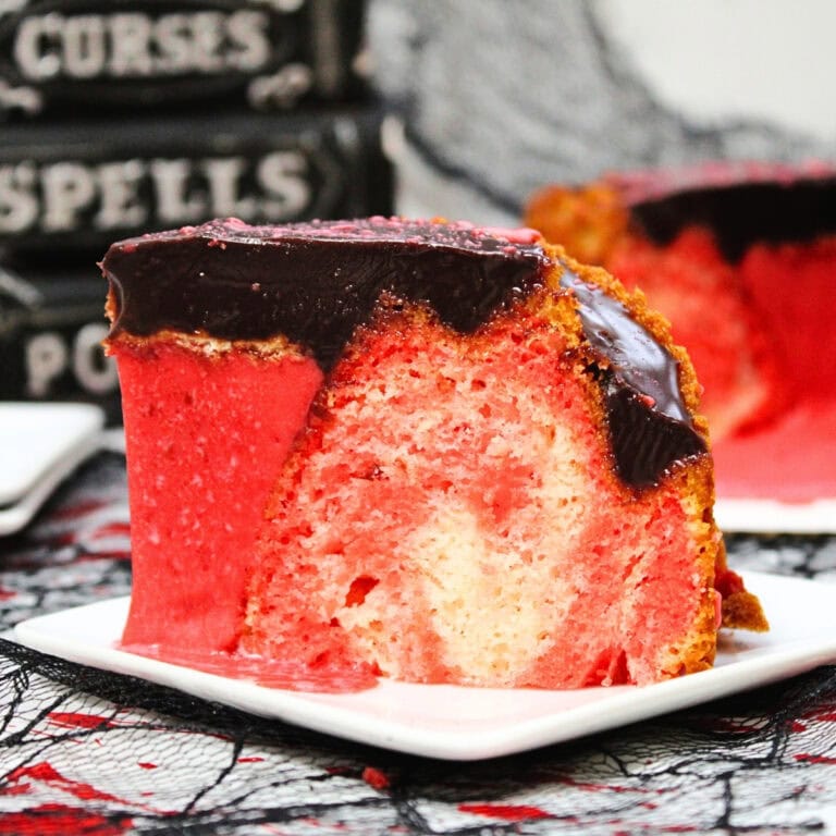 A slice of marbled red and white cake with chocolate icing on a white plate.