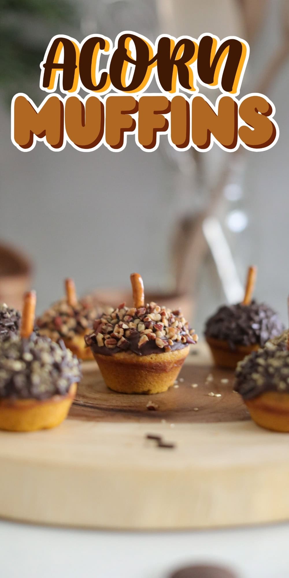Mini muffins decorated as acorns with pretzel stems on a wooden board.