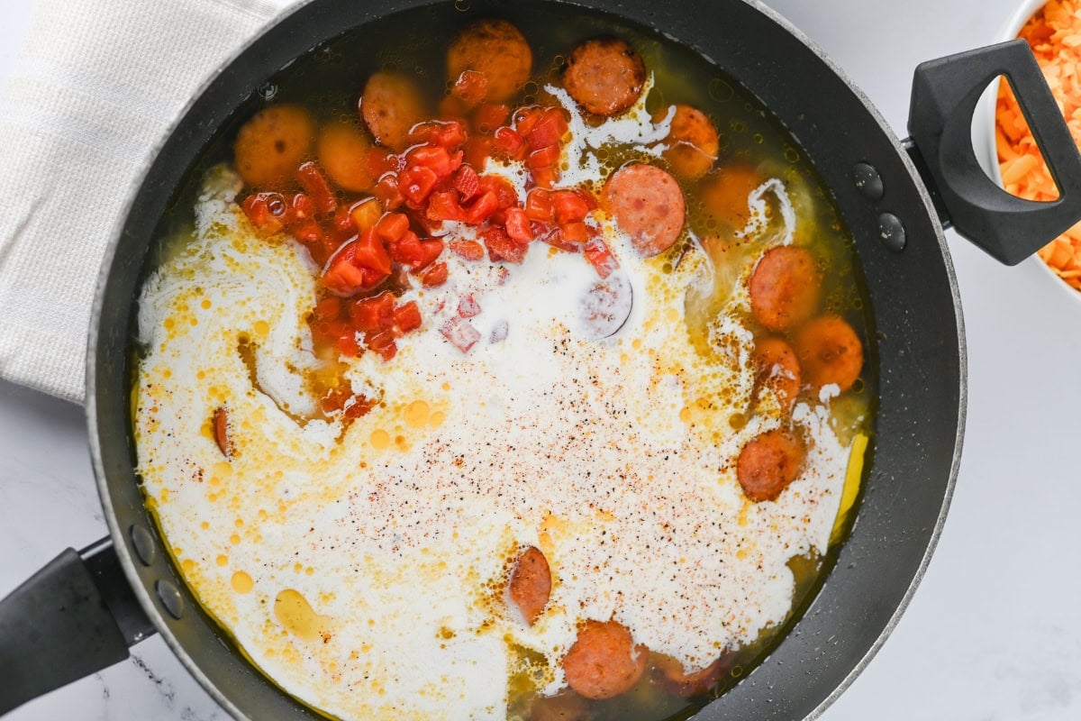 Sliced sausage, diced tomatoes, and cream simmering in a black skillet.