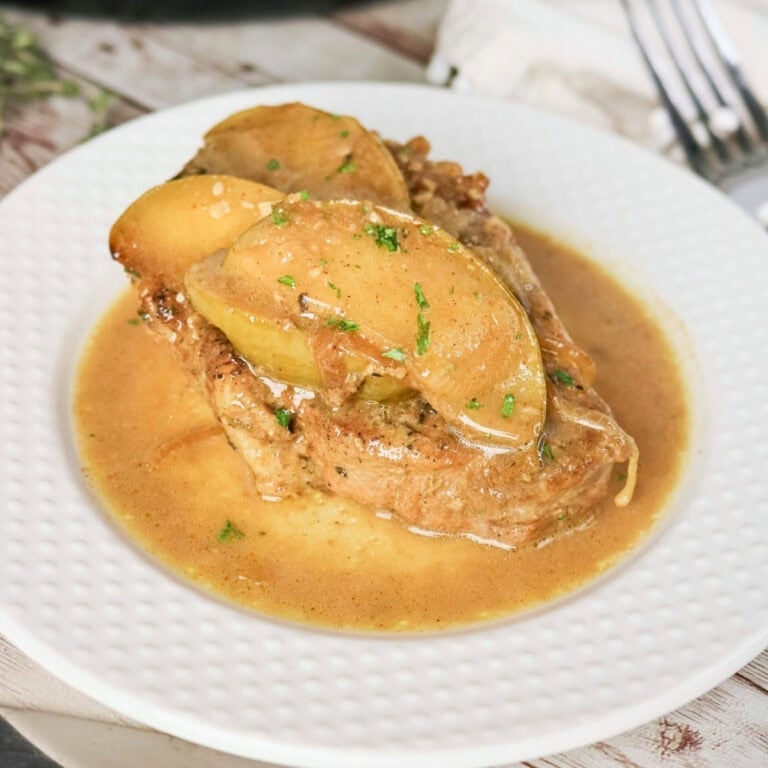 Pork chop topped with cooked apples and sauce on a white plate.