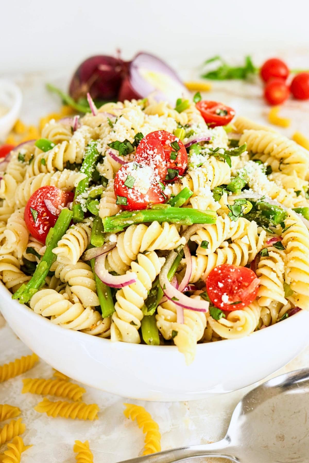 Pasta salad with tomatoes, asparagus, red onion, herbs, and sprinkled parmesan.