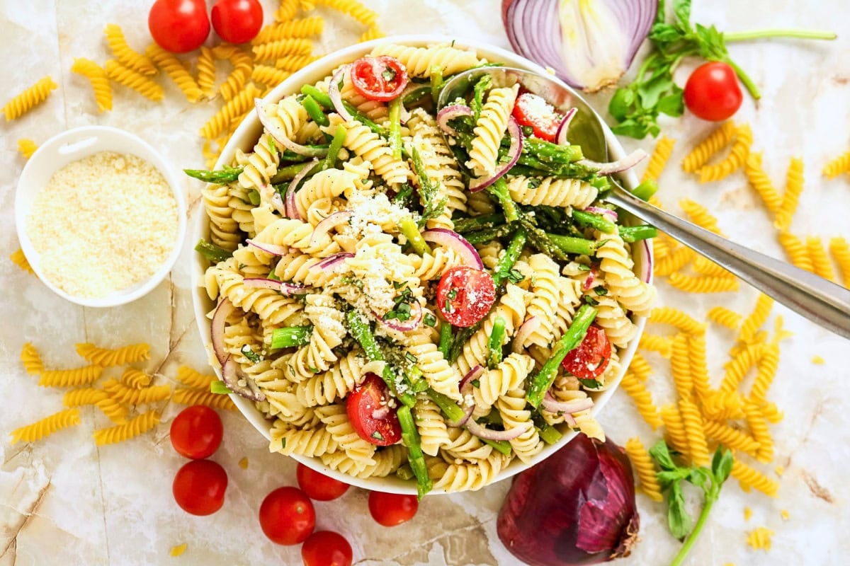 A bowl of rotini pasta salad with tomatoes, asparagus, and parmesan cheese.