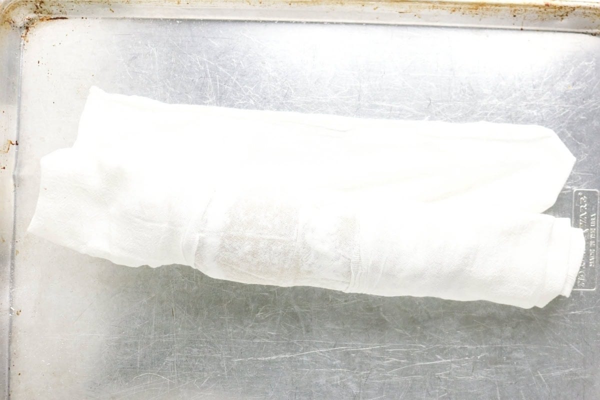 A rolled-up white towel on a metal baking sheet.