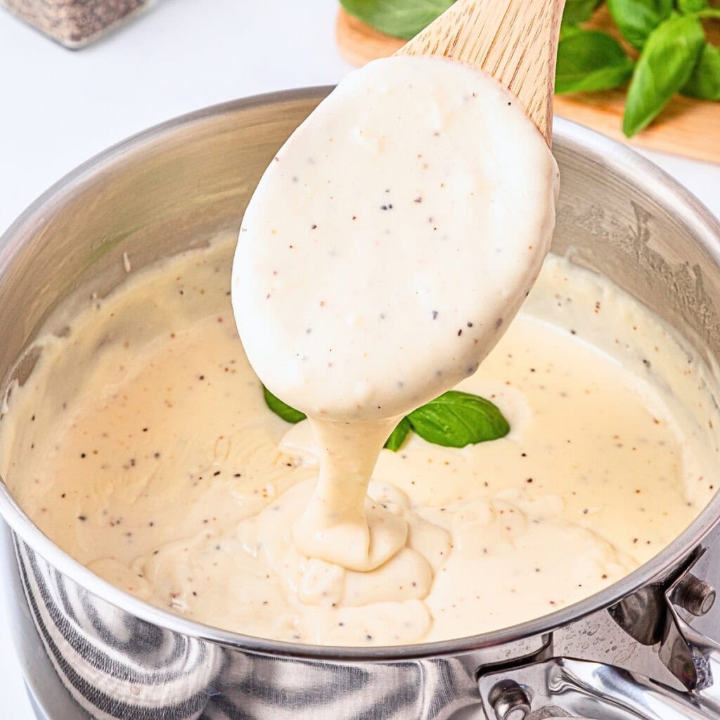 Creamy white sauce being stirred with a wooden spoon in a saucepan.