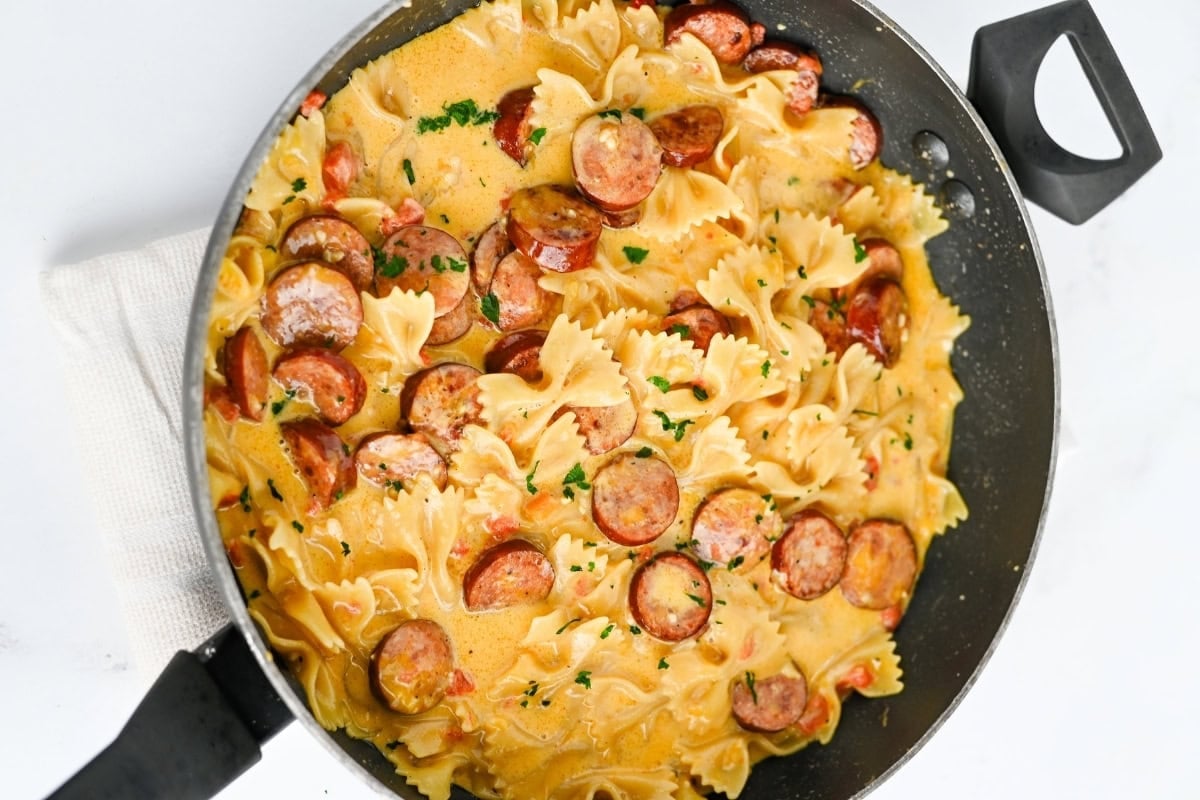 Farfalle pasta with sausage in a creamy sauce, garnished with herbs in a pan.