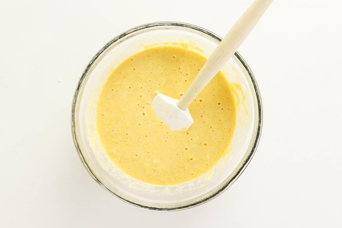 Bowl of yellow batter with a white spatula on a white background.