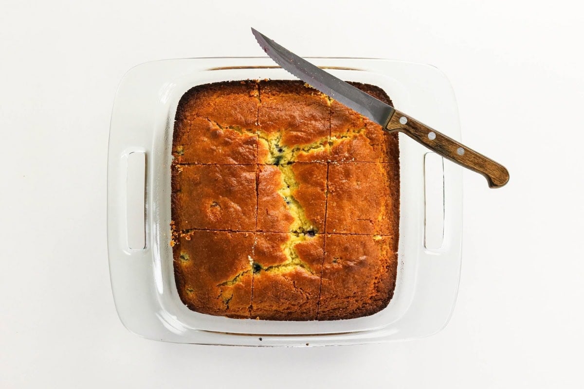 Golden cornbread in a glass dish, sliced, with a knife resting on top.