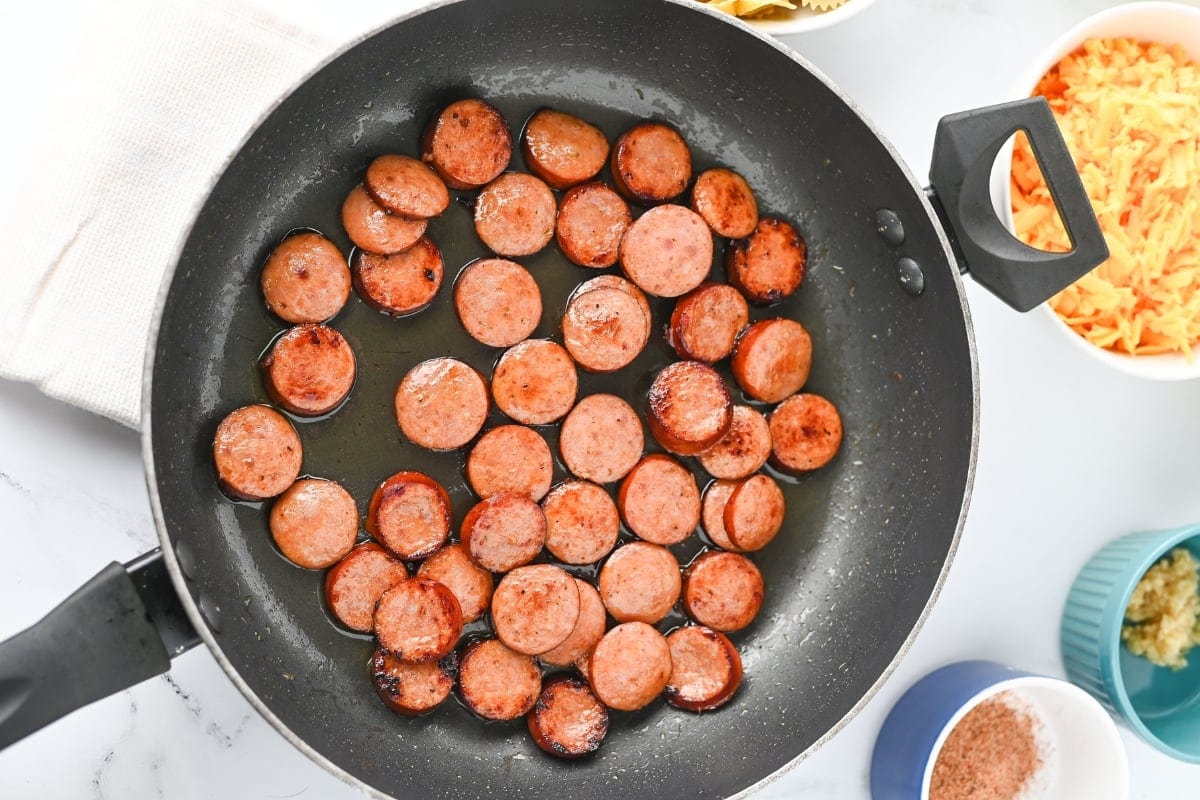 Sliced sausage cooking in a black skillet on a white countertop.