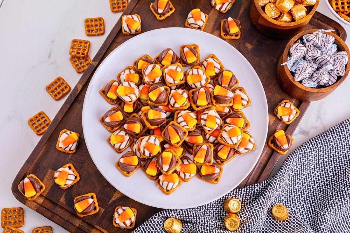 Plate of pretzel snacks topped with chocolate and candy corn on a wooden board.