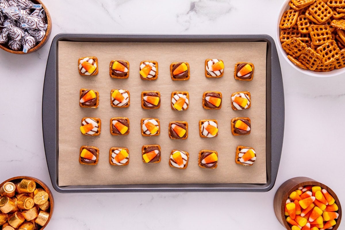 Baking tray with pretzel treats topped with chocolate and candy corn.