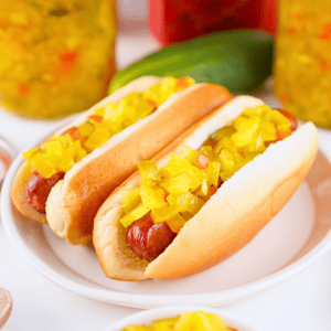 Two hot dogs with yellow relish on a white plate.