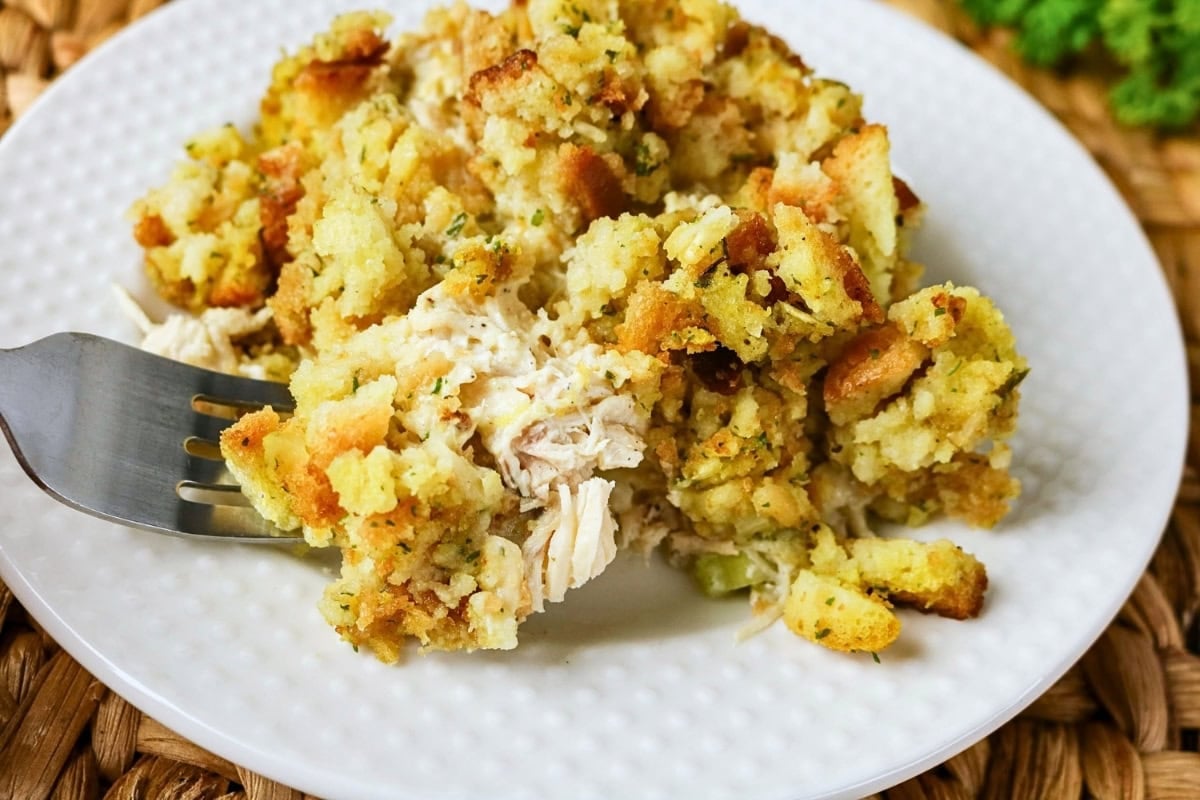 A fork beside a serving of chicken and stuffing casserole on a white plate.
