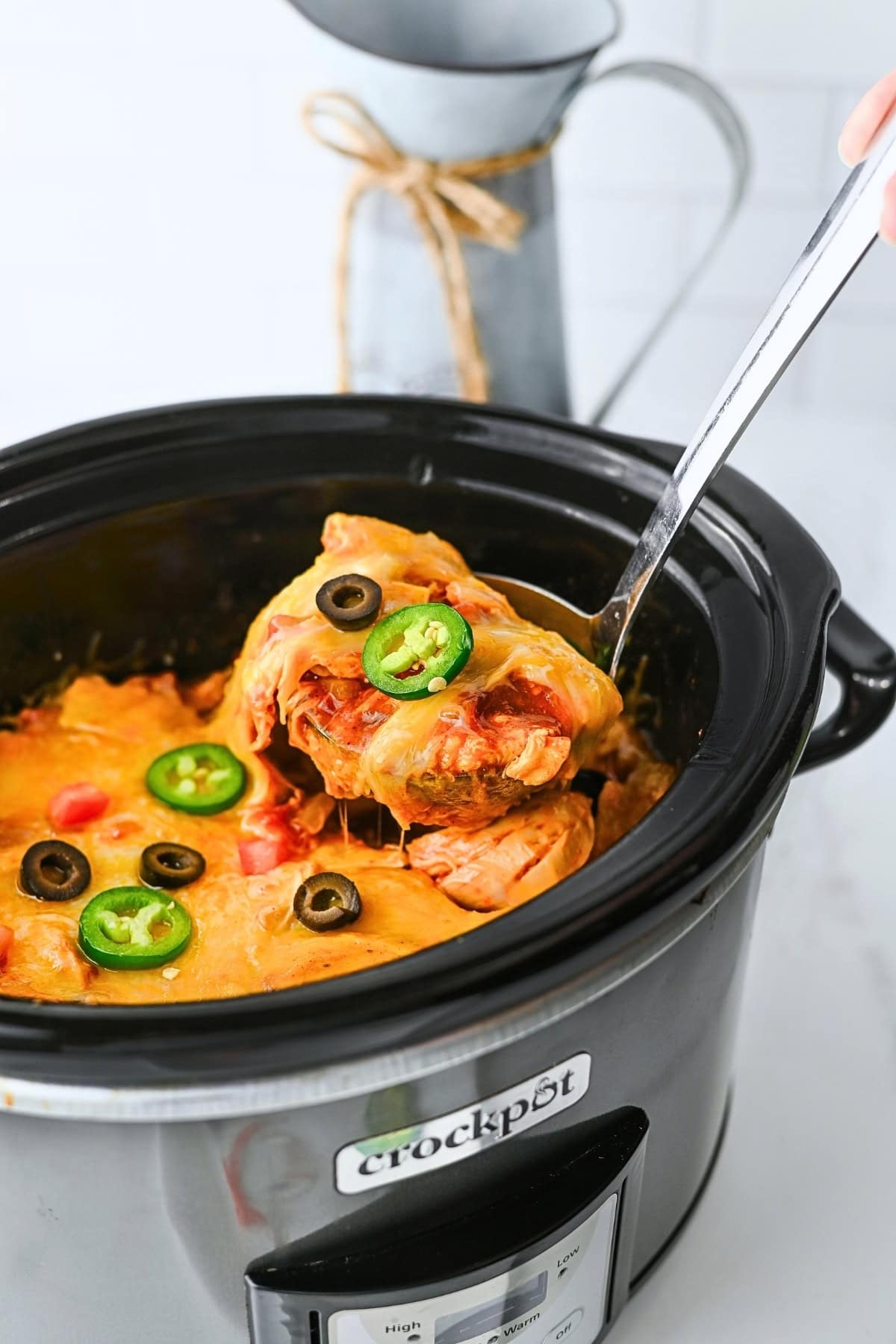 Cheesy casserole with jalapeños and olives in a black Crockpot being served.