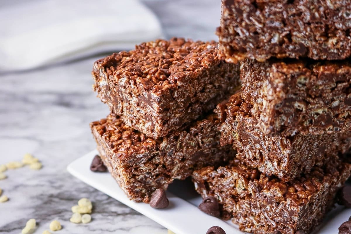 Stacked chocolate rice crispy treats on a plate with scattered chocolate chips.