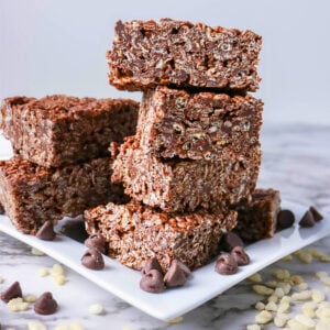 Stacked chocolate rice crispy treats on a white plate with chocolate chips.
