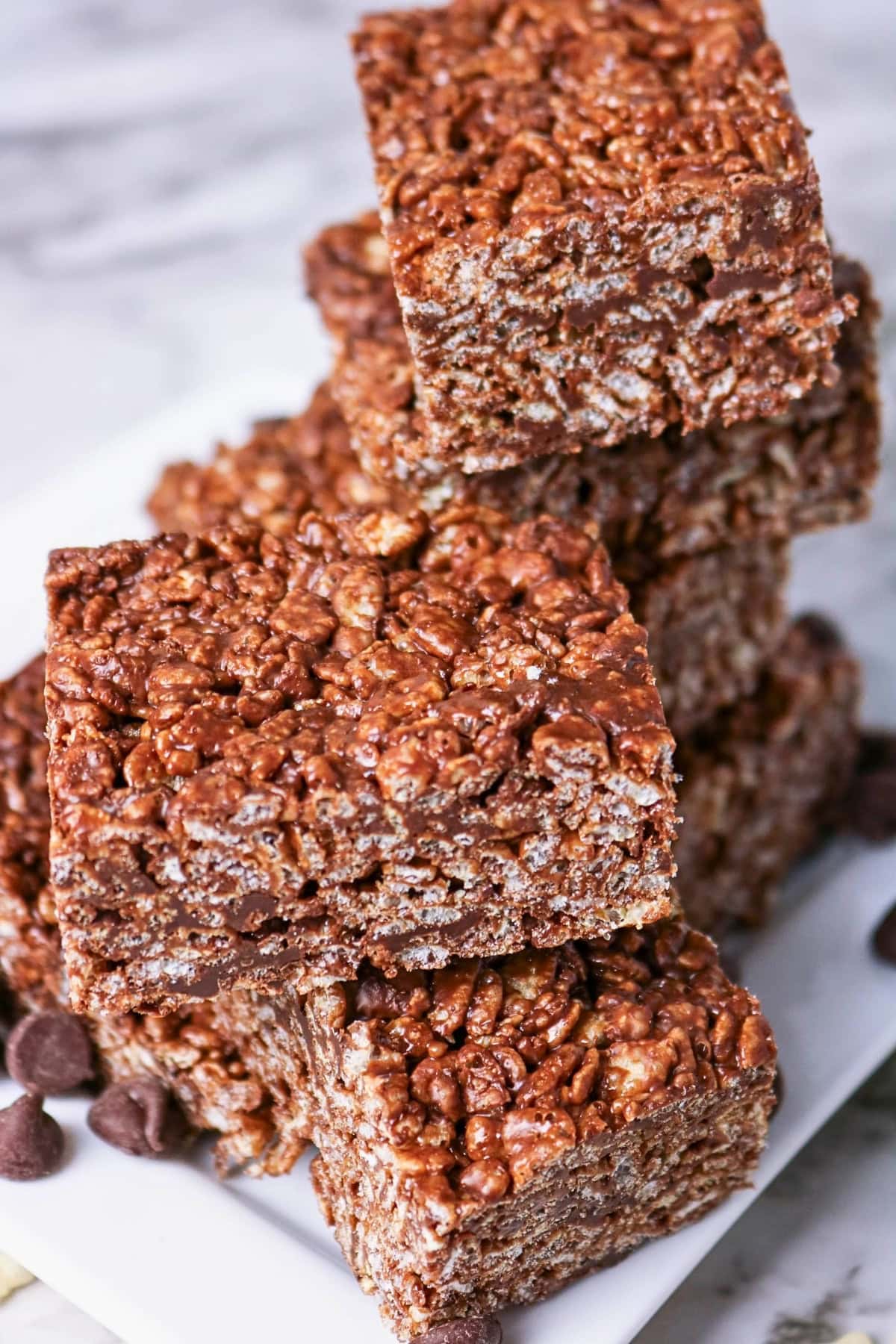 Chocolate rice crispy treats stacked on a plate with chocolate chips nearby.