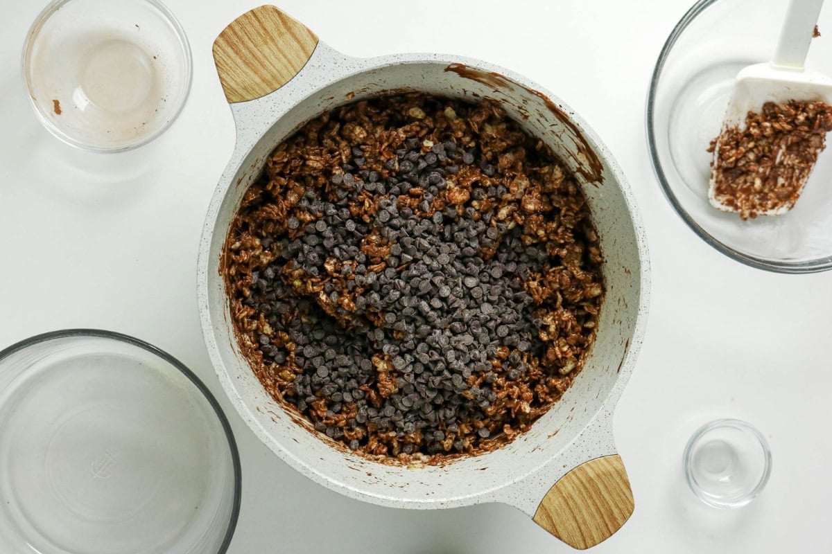 Mixing bowl with oats and chocolate chips, surrounded by empty glass bowls.