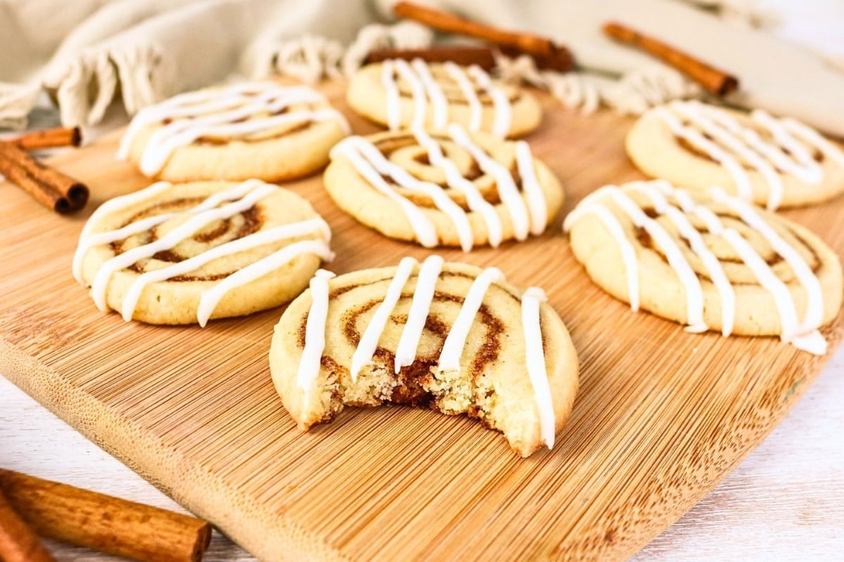 Seven cinnamon cookies with icing; one has a bite taken out of it.
