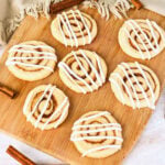 Seven cinnamon swirl cookies with white icing on a wooden board.